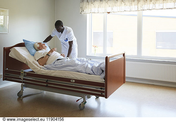 Male nurse adjusting senior man's bed in hospital ward