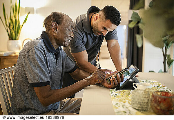 Male nurse assisting senior man in using digital tablet and smart phone at nursing home