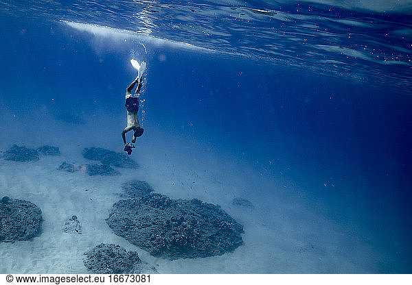 male ocean photographer holding breathe and diving deep to ocean floor