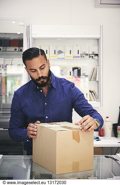 Male owner packing box at counter in electronics store