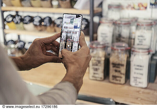 Male owner photographing jars through smart phone at organic store