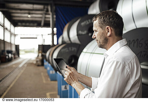 Male owner using digital tablet while standing in factory
