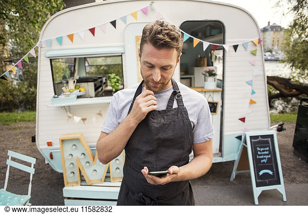 Male owner using smart phone while standing on street against food truck