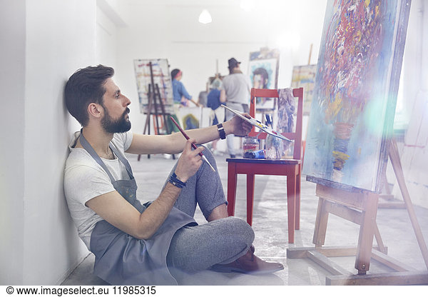 Male painter painting  examining painting in art class studio