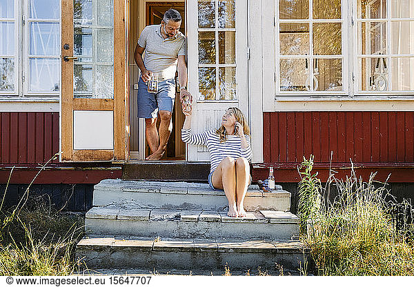 Male partner giving glass of water to woman while standing in doorway at log cabin