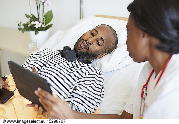 Male patient looking at digital tablet held by female doctor in hospital ward