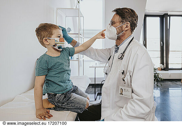 Male pediatrician with protective face mask checking boy in medical examination room