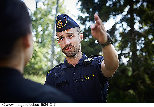 Male police officer gesturing while directing woman outdoors