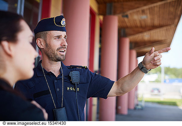 Male police officer pointing while directing coworker outside police station