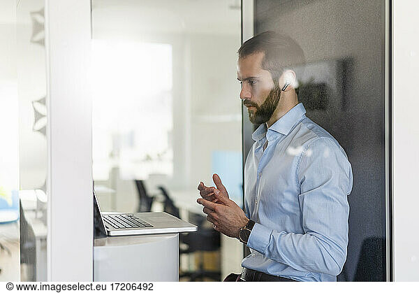 Male professional having discussion on video call over laptop in telephone booth at office