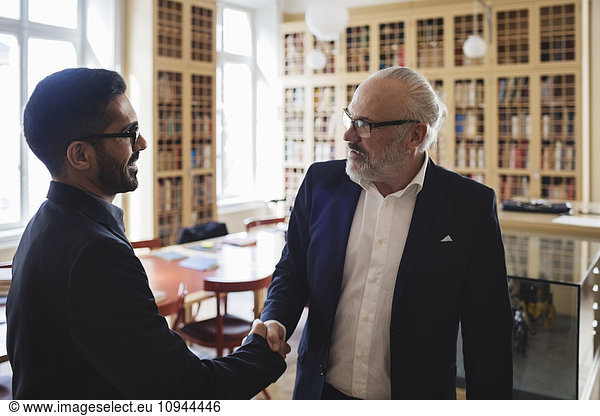 Male professional shaking hand with senior man in law library