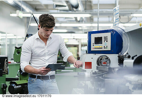 Male professional using digital tablet while standing by machinery equipment in industry