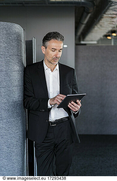 Male professional using digital tablet while standing by wall in office