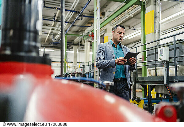 Male professional using digital tablet while walking in factory
