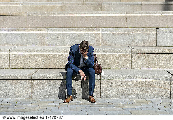 Male professional with head in hand sitting on steps
