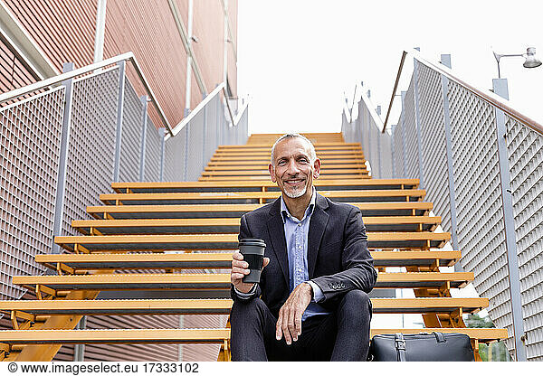 Male professional with reusable cup sitting on staircase near building