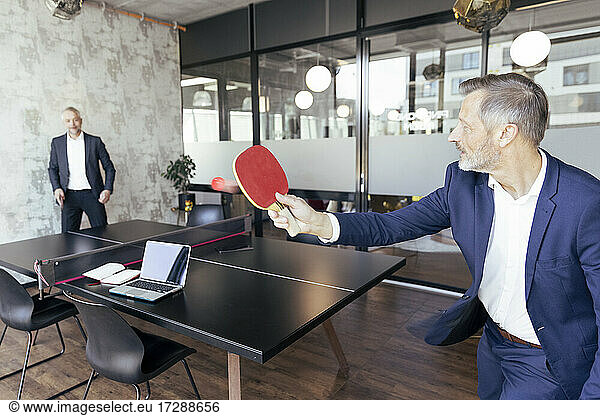 Male professionals playing table tennis at office