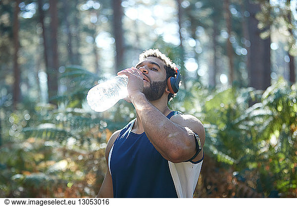 Male runner drinking bottled water in sunlit forest