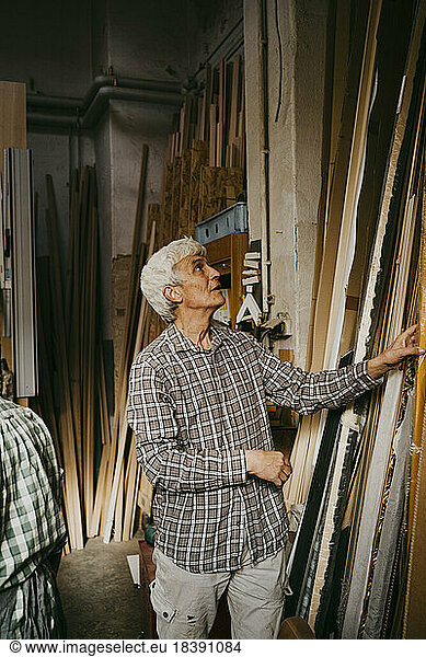 Male senior entrepreneur selecting wood while standing at workshop