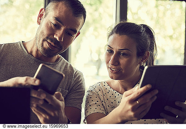 Male showing mobile phone to female partner in cafe