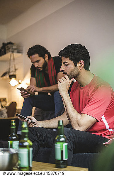 Male soccer fans using mobile phone while watching match at home