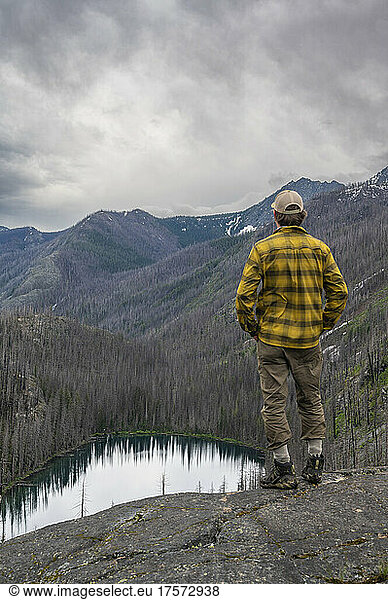 Male stands above an alpine lake surrounded by burned trees