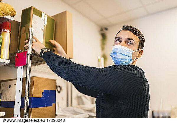 Male store owner wearing protective face mask while removing box from shelf