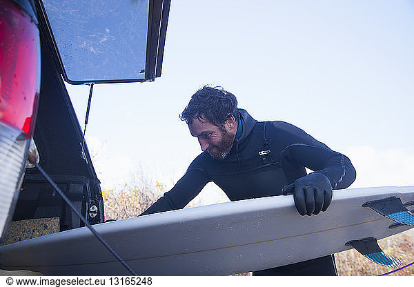 Male surfer removing surfboard from car boot  Gloucester  Massachusetts  USA