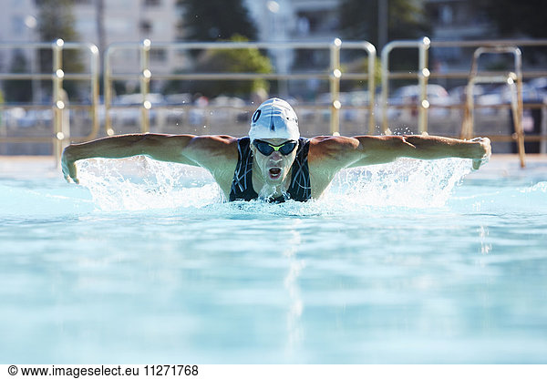 Male swimmer athlete doing butterfly stroke swimming in swimming pool