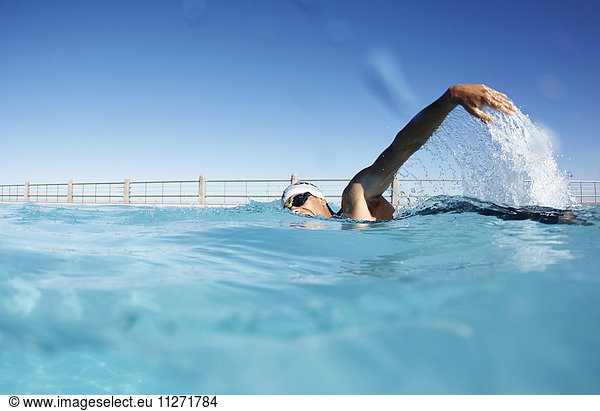 Male swimmer athlete swimming in sunny swimming pool