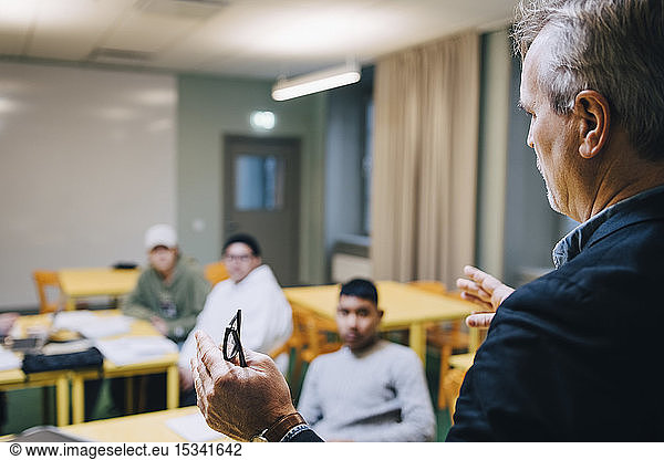 Male teacher gesturing while teaching students in classroom