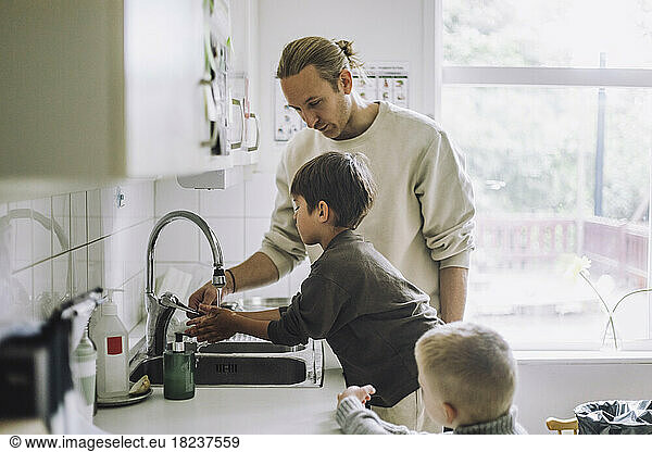 Male teacher guiding boys to wash hands near sink at child care center