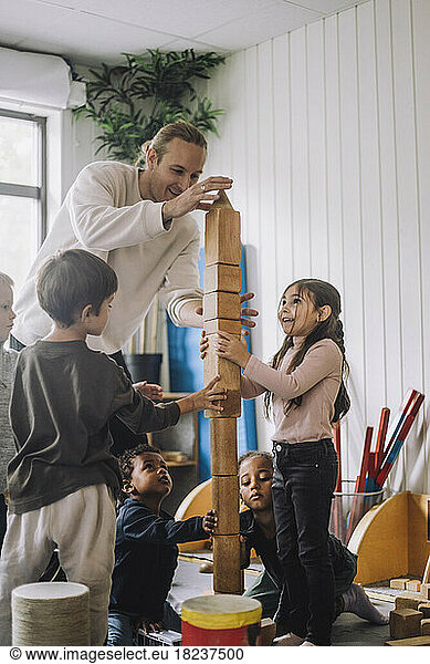 Male teacher guiding children stacking wooden toy blocks at kindergarten