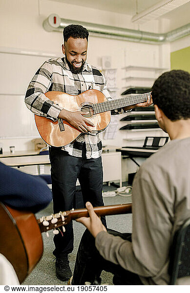 Male teacher playing guitar with students in music class at high school