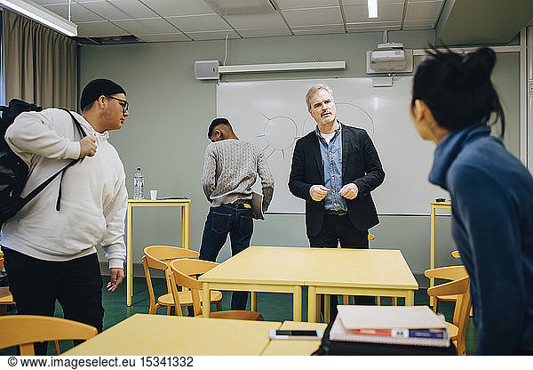 Male teacher talking to female student standing in classroom