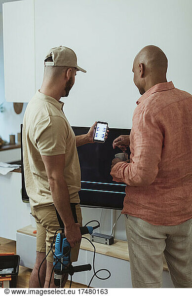 Male technician showing app on smart with man in living room