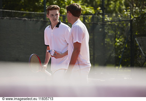 Male tennis players with tennis rackets talking on sunny tennis court