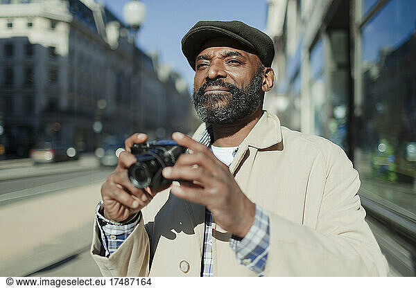 Male tourist with beard using digital camera on sunny city sidewalk