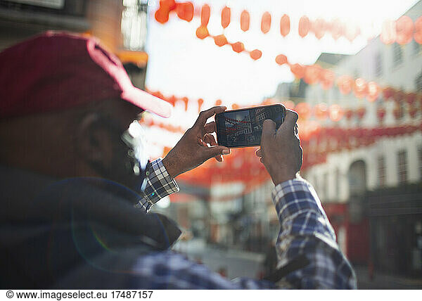 Male tourist with camera phone photographing paper lanterns in city