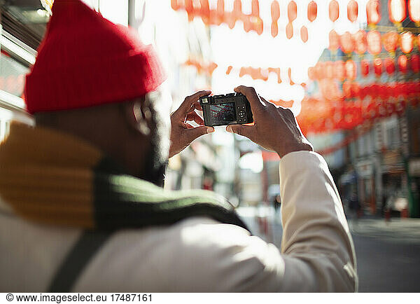 Male tourist with digital camera photographing paper lanterns in city