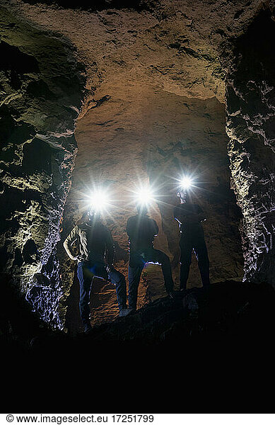 Male tourists with illuminated headlamps standing in cave