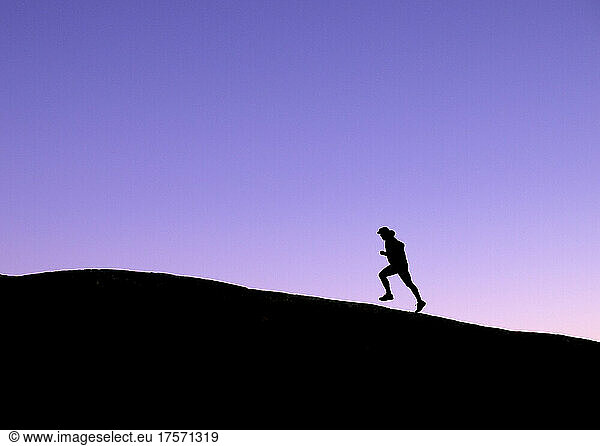 male trail runner silhouetted against purple evening sky
