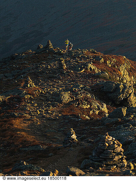 Male trail runners running across rocks at sunrise in mountains