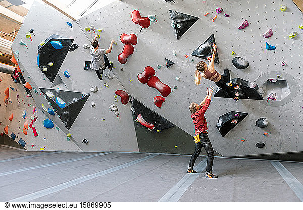Male trainer training woman and man in wall climbing at gym