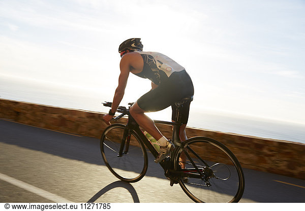 Male triathlete cyclist cycling on sunny ocean road