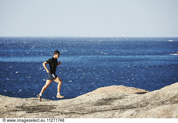Male triathlete runner running along rocky ocean trail