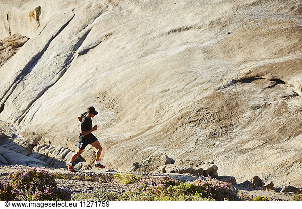 Male triathlete runner running on sunny rocky trail