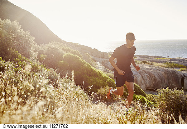 Male triathlete runner running on sunny rocky trail