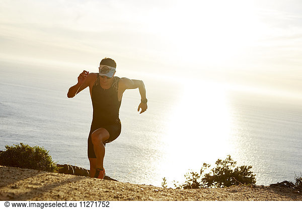 Male triathlete runner running uphill on sunny ocean trail