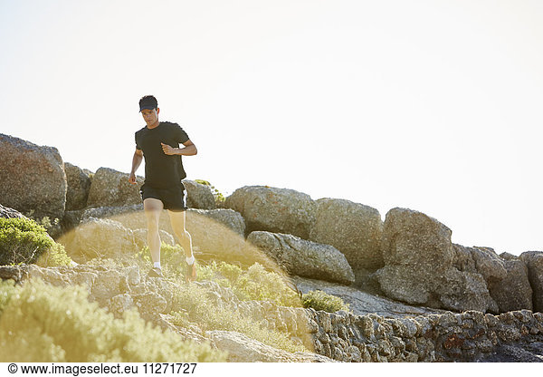 Male triathlete running on sunny rocky trail